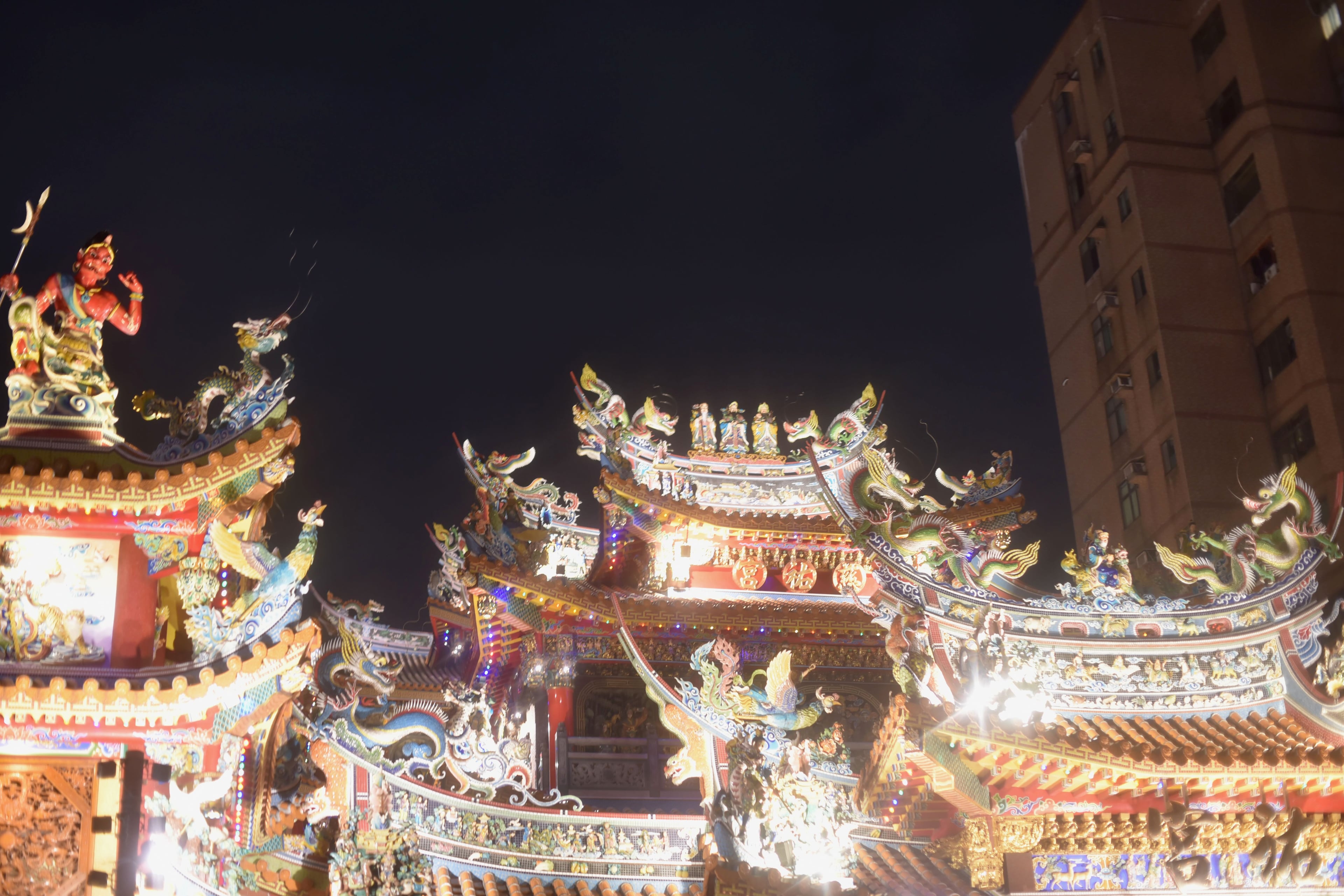 A Taipei temple at night, intricate dragon and figure carvings lit on the roofs